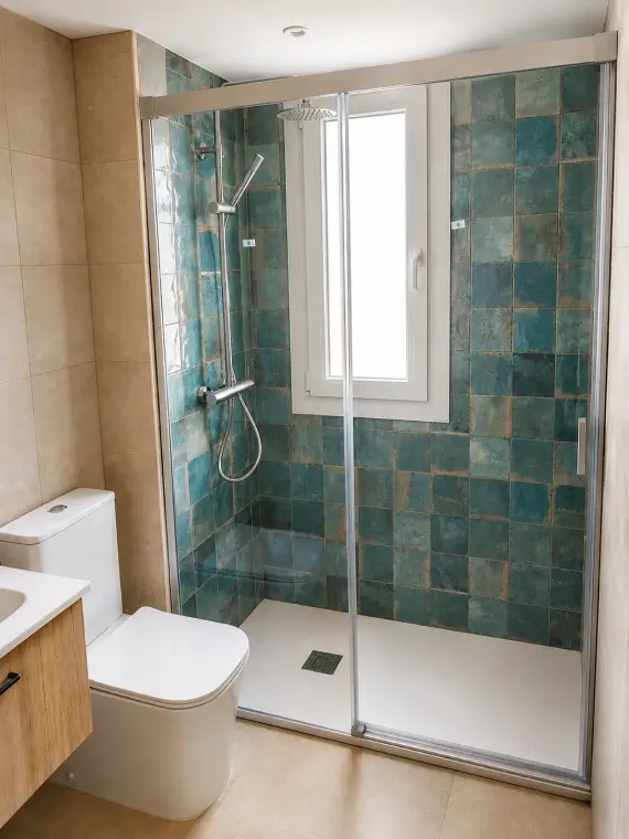 Baño reformado con azulejos en tonos verdes y ducha con mampara.